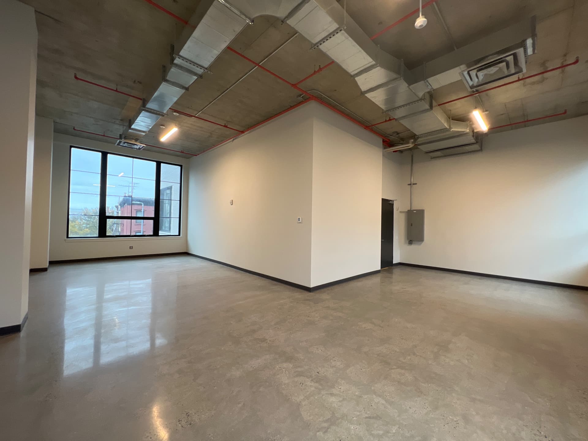 Empty loft floor at 497 Carroll Street with polished concrete floor, exposed ductwork and a black steel window