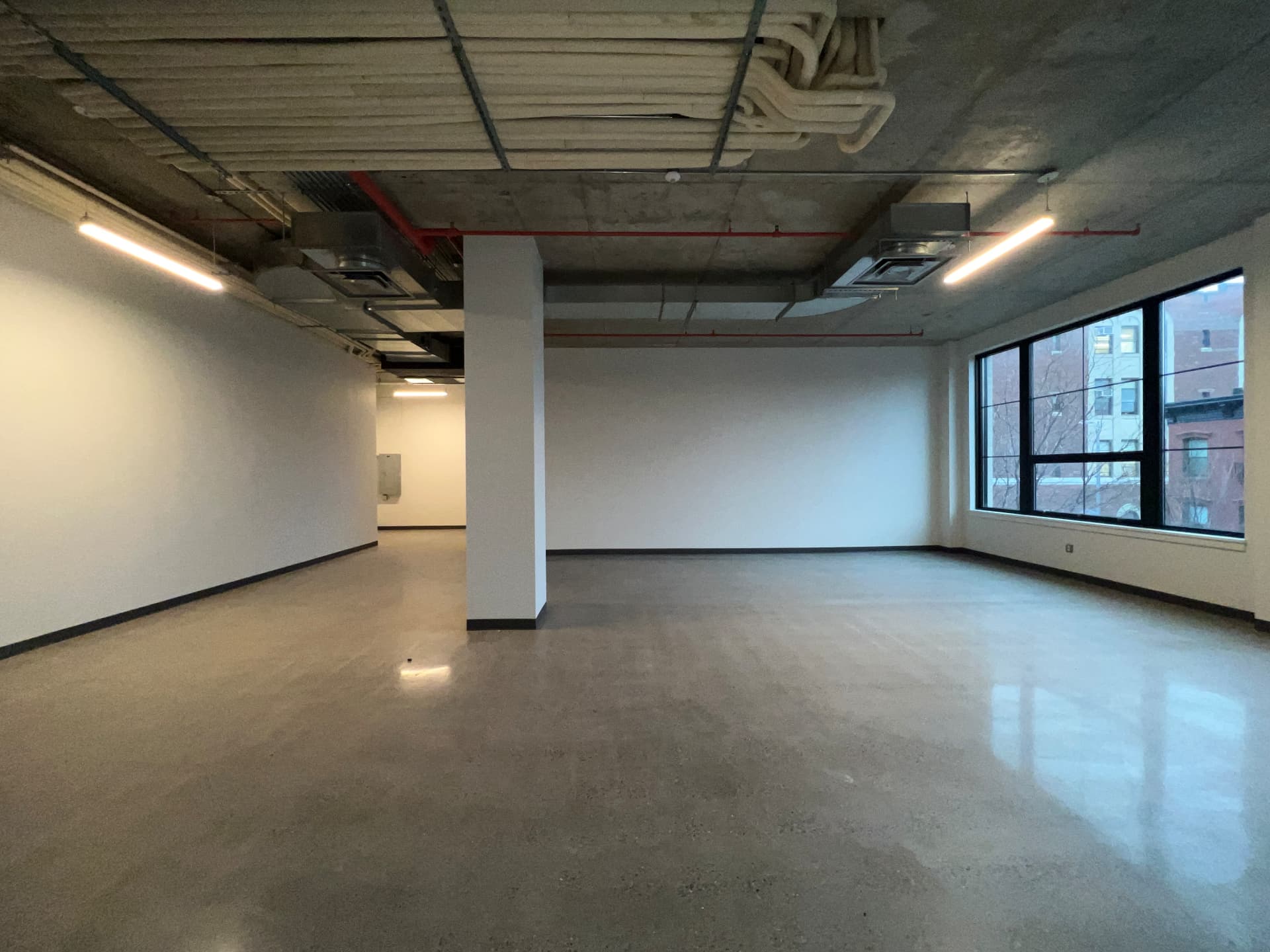 Wide open loft plate with a central column, exposed services and daylight from black steel windows